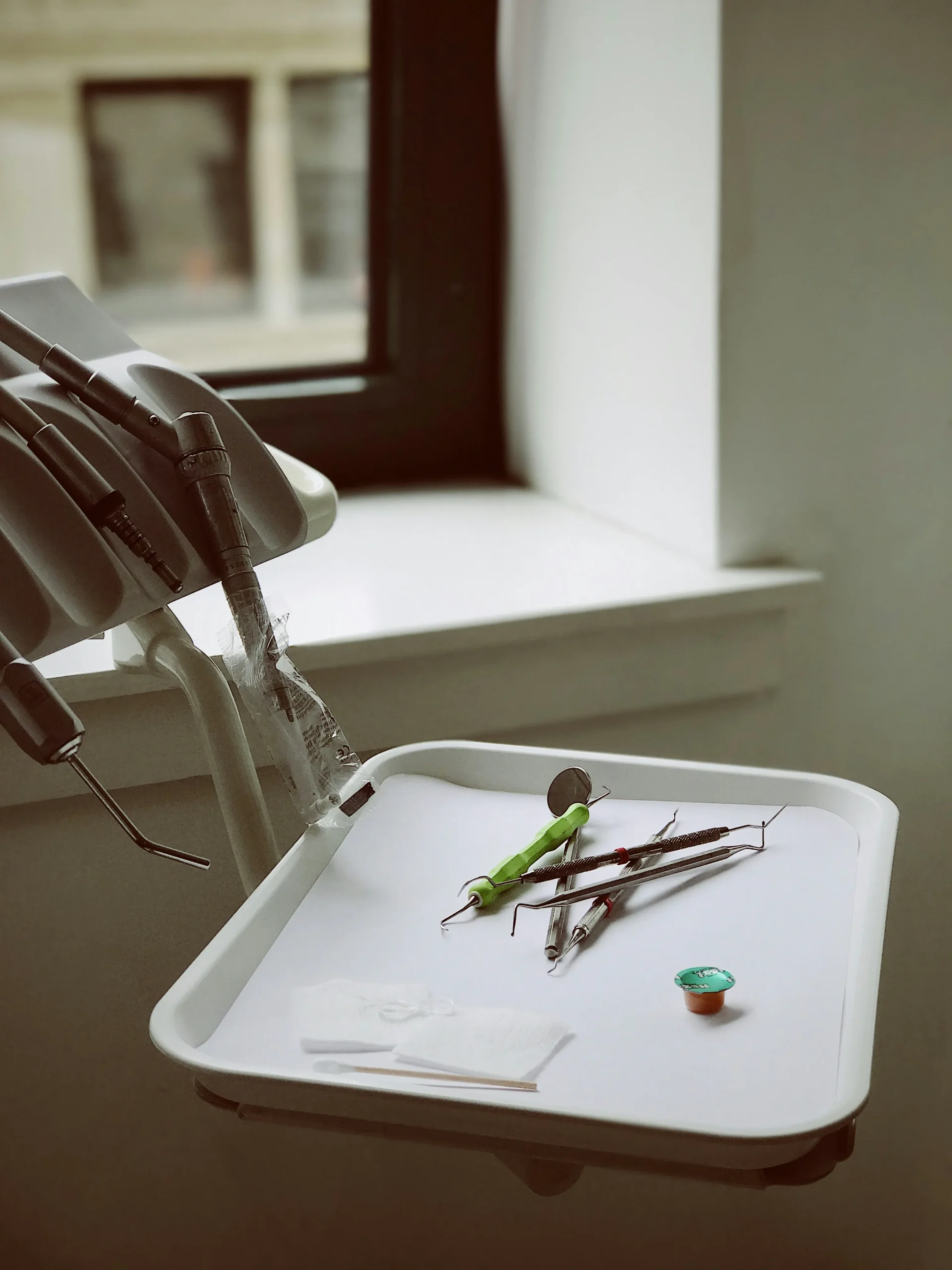 Bandeja clínica con instrumental de exploración, gasas y piezas de mano rotatorias preparadas junto a la ventana en el gabinete de la clínica dental Dentelier en Alicante.