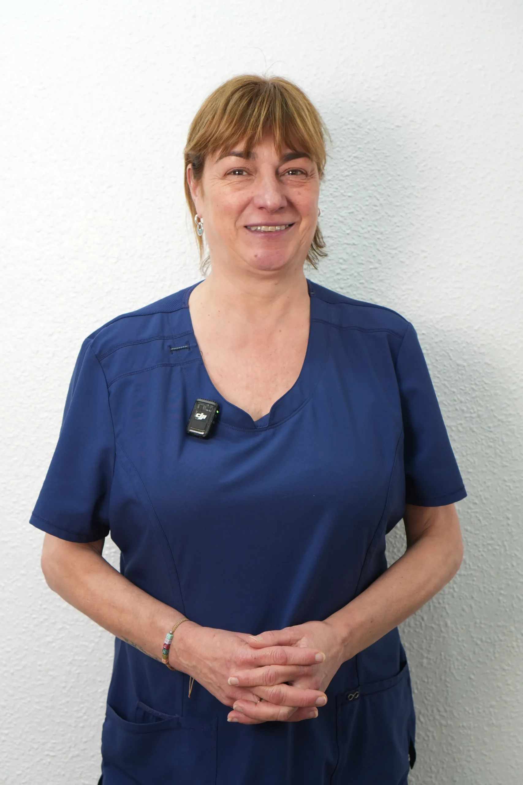 Retrato de Isabel, especialista de la clínica dental Dentelier en Alicante, posando con las manos cruzadas y uniforme sanitario azul marino sobre un fondo blanco.