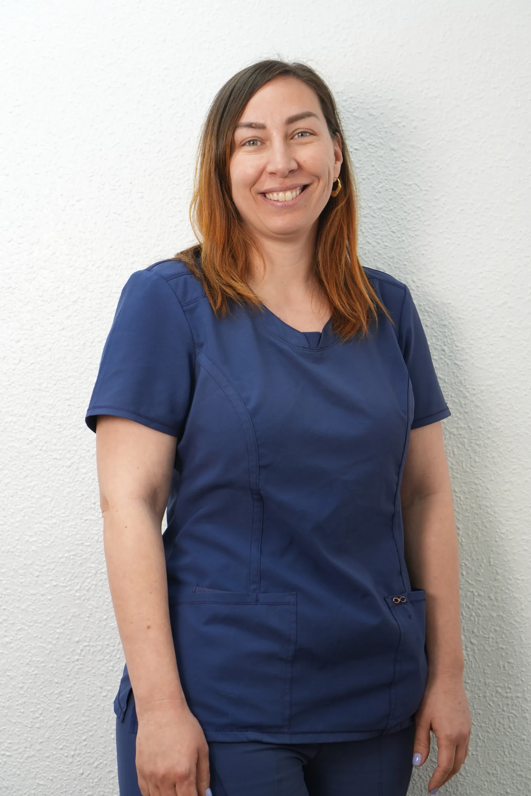 Retrato de Virginia, miembro del equipo de la clínica dental Dentelier en Alicante, sonriendo con uniforme sanitario azul marino sobre un fondo blanco.
