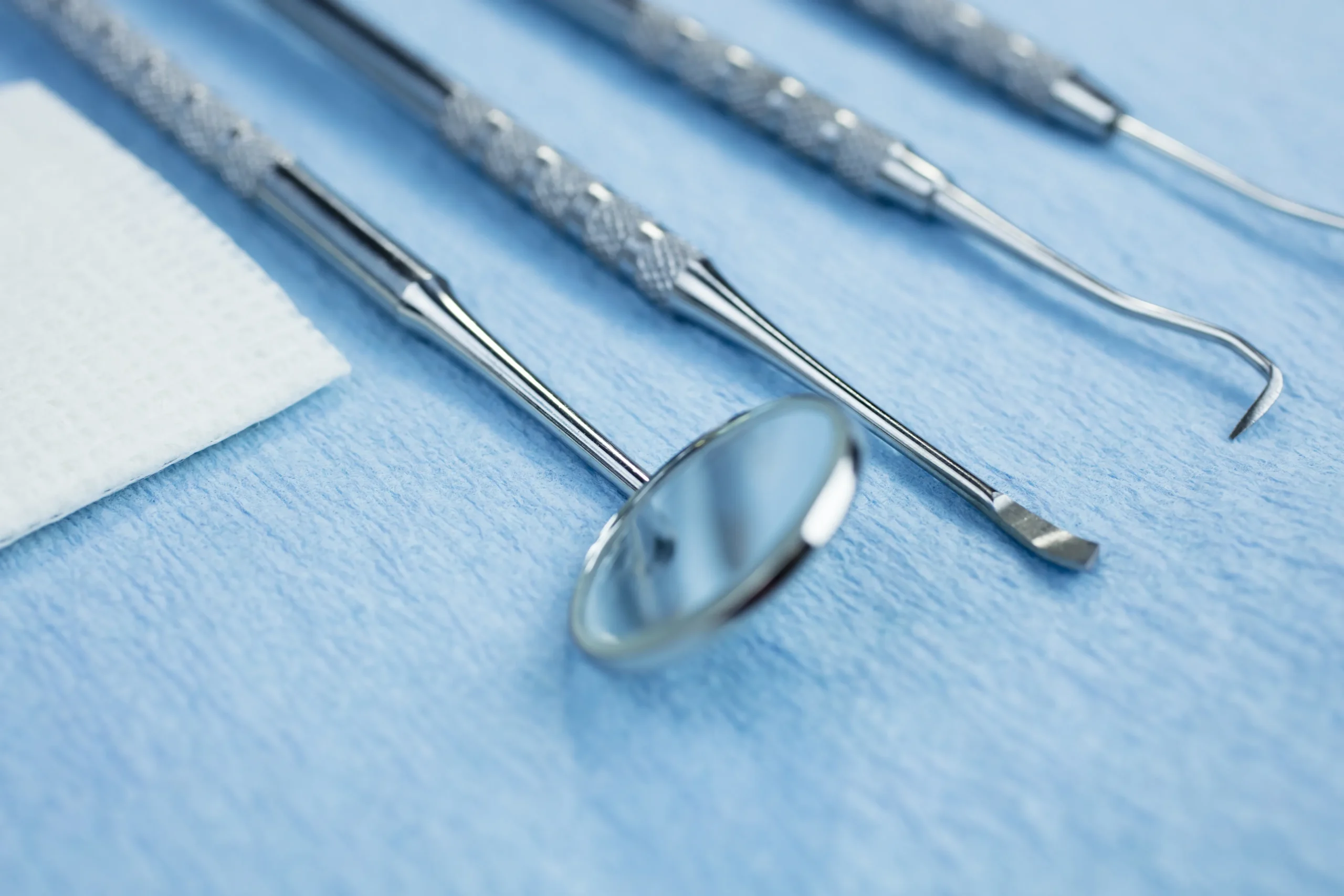 Kit de exploración odontológica que incluye espejo intraoral, sonda de exploración y excavador sobre un paño clínico azul en la clínica dental Dentelier en Alicante.